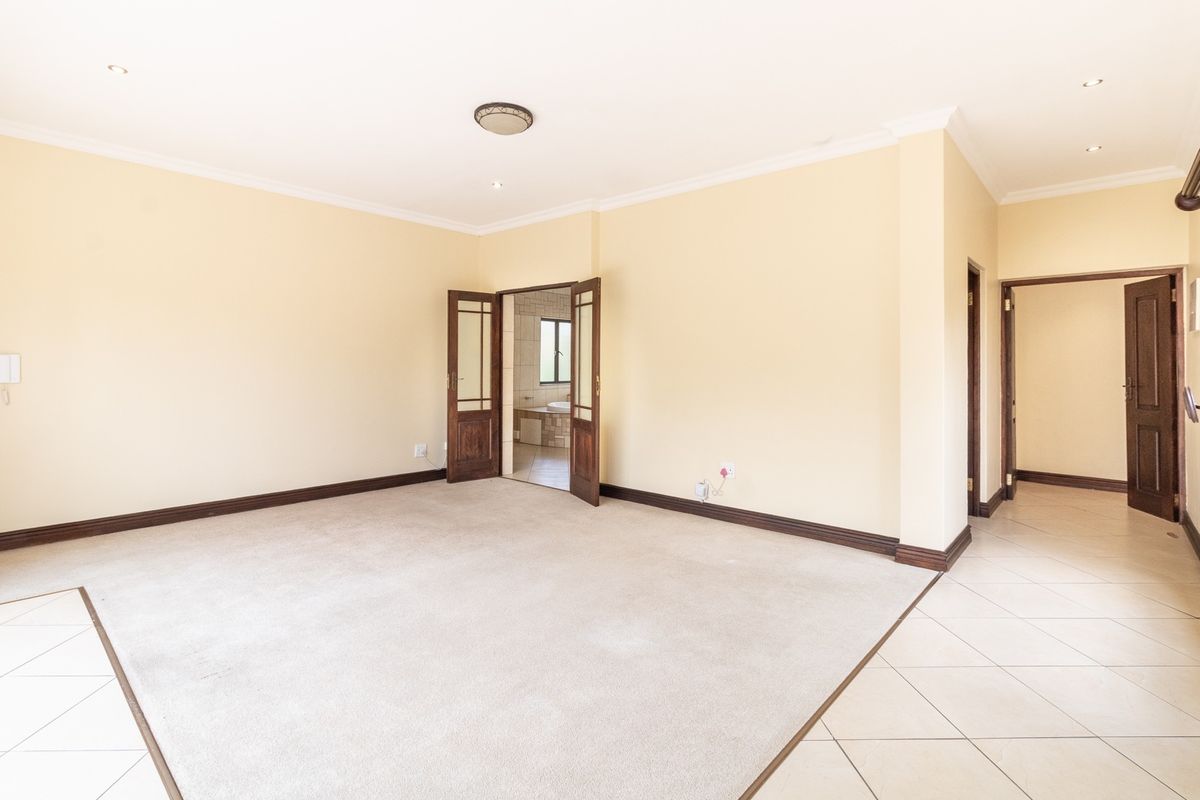 Spacious, empty bedroom featuring neutral carpet and tiled flooring, with direct access to an en-suite bathroom through double timber doors.