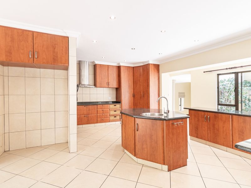 Spacious kitchen featuring wooden cabinetry, granite countertops, a central island with a sink, and tiled flooring throughout.