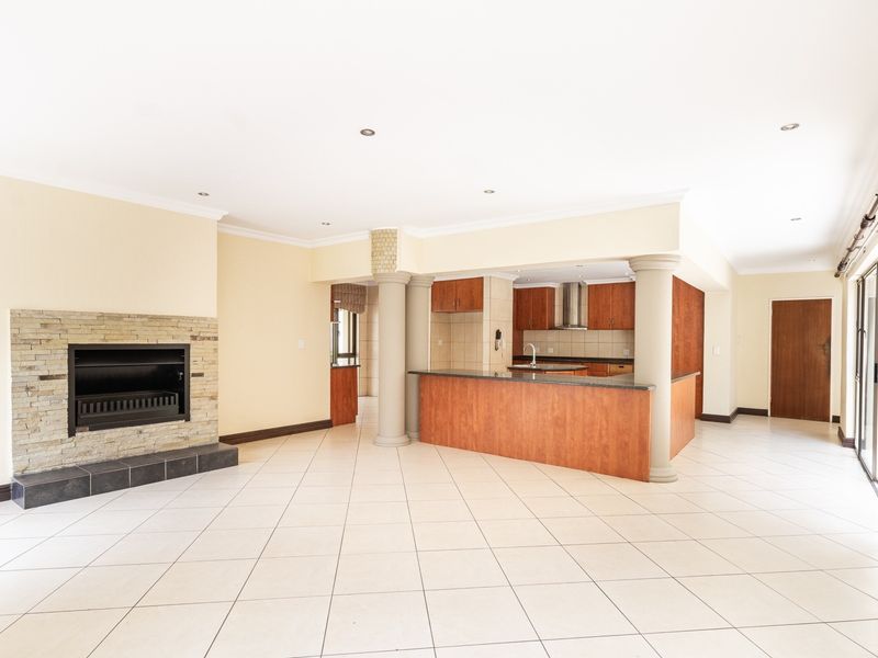 Spacious open-plan living and kitchen area featuring a stone-clad fireplace, tiled flooring, and a functional kitchen with built-in cabinetry and island.