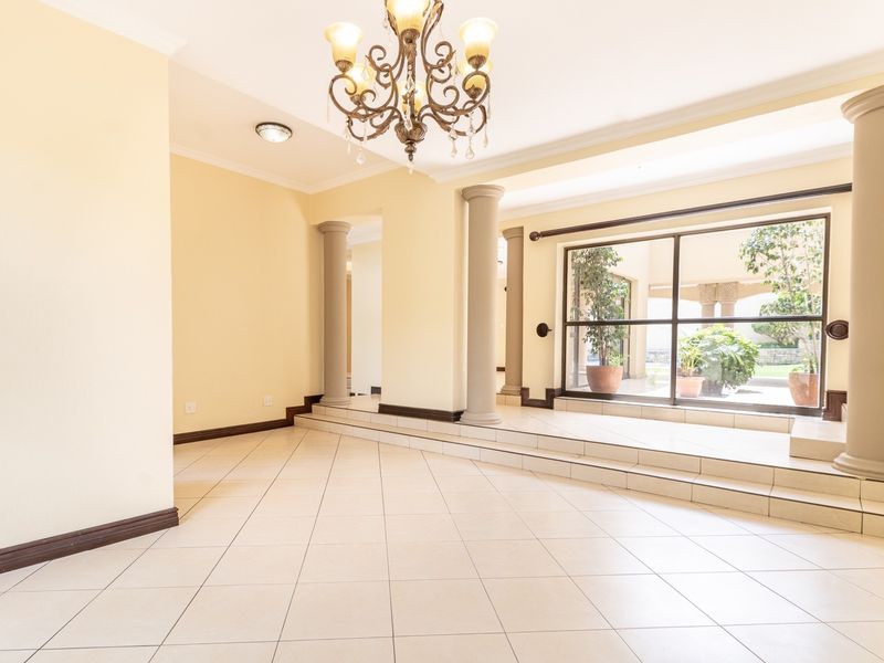 Spacious living area featuring tiled floors, decorative columns, a raised platform, and a large sliding glass door providing natural light and garden access.