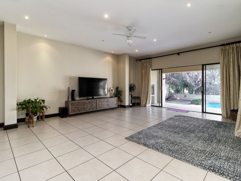 Spacious living room featuring neutral tiled flooring, recessed lighting, and large sliding glass doors providing seamless access to the outdoor patio and pool area.