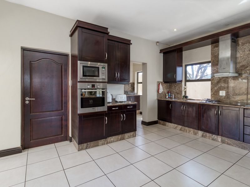 A well-maintained kitchen featuring dark wood cabinetry, granite countertops, built-in appliances, and tiled flooring, with an adjacent scullery area.