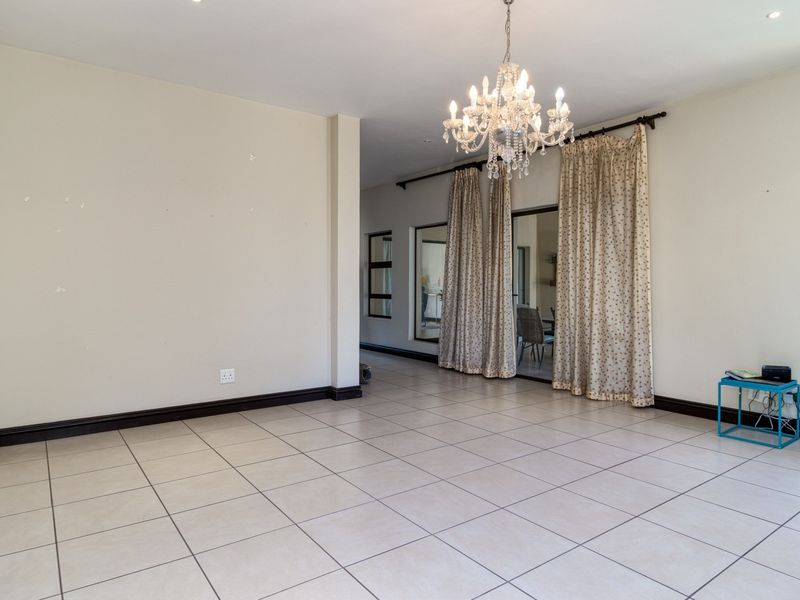 Spacious living area featuring neutral tiled flooring, recessed lighting, a decorative crystal chandelier, and sliding glass doors leading to an adjacent space.