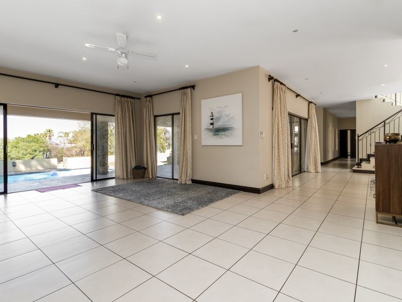 Spacious open-plan living area featuring neutral tiled floors, recessed lighting, and large sliding glass doors providing seamless access to the outdoor pool area.