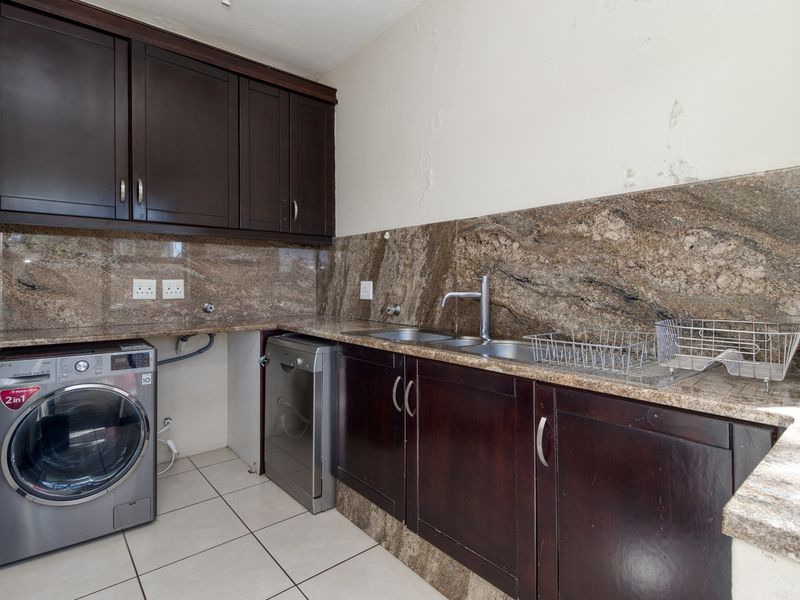 Laundry area featuring dark wood cabinetry, granite countertops, and a stainless steel double sink with visible wall surface damage.