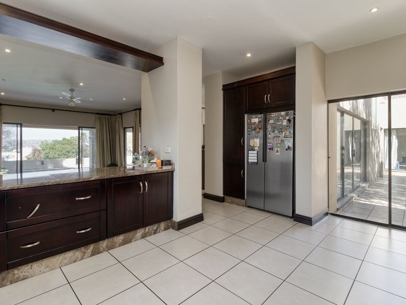 A spacious kitchen featuring dark wood cabinetry, granite countertops, tiled flooring, and direct access to an outdoor patio area through sliding glass doors.