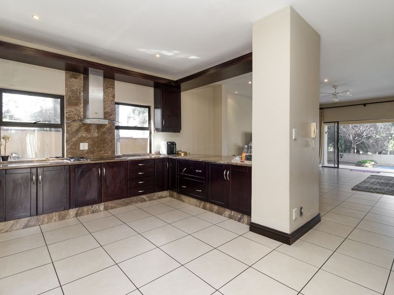 Open plan kitchen featuring dark wood cabinetry, granite countertops, and stainless steel appliances, flowing into a spacious living area with access to the patio.