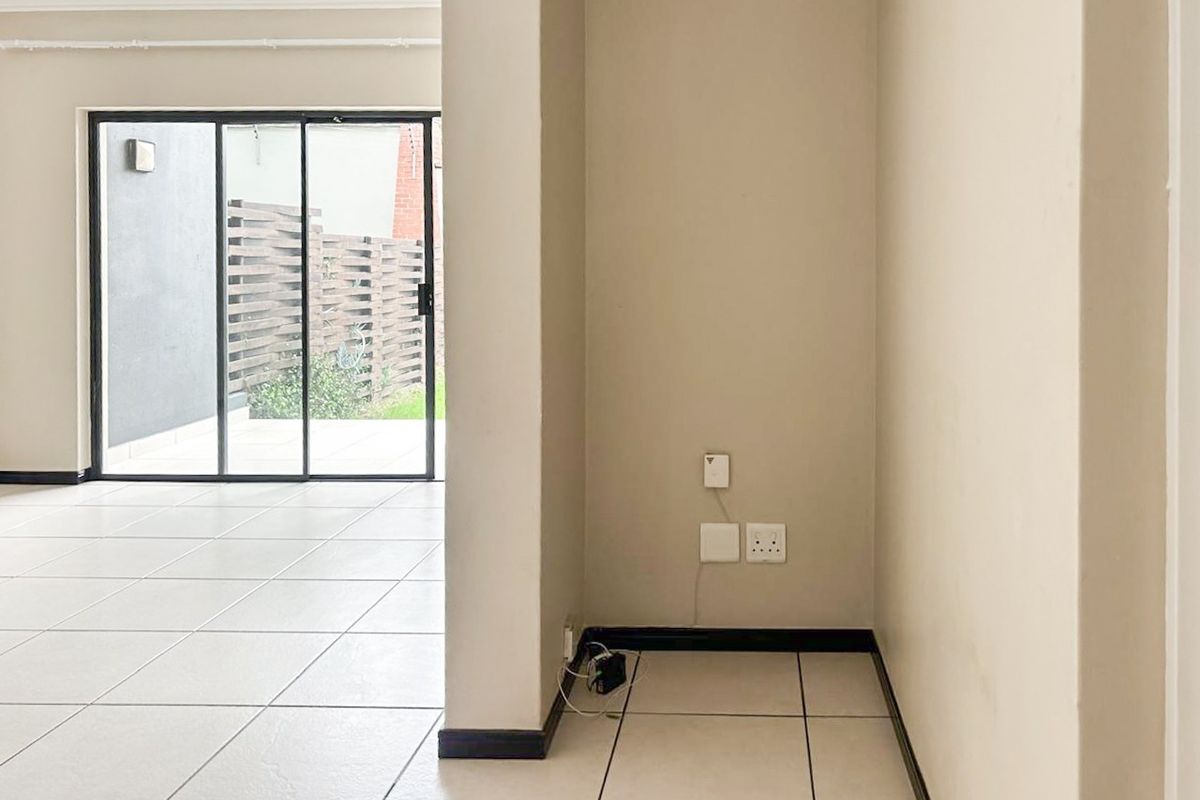 An empty, open-plan living area featuring neutral tiled flooring and a large sliding glass door providing access to the outdoor space.