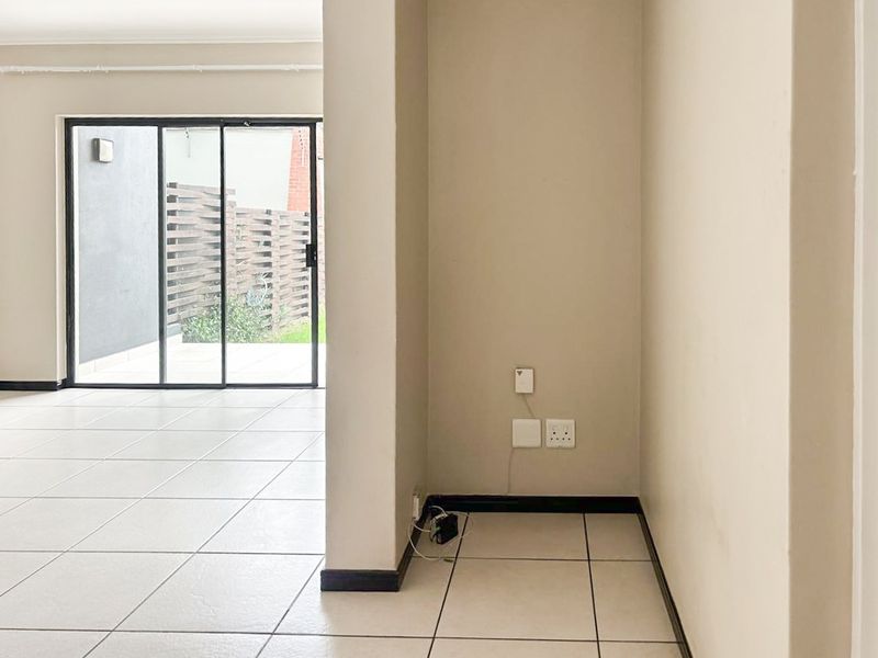 An empty, open-plan living area featuring neutral tiled flooring and a large sliding glass door providing access to the outdoor space.
