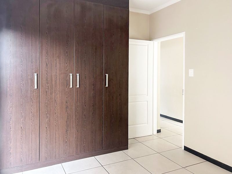 A clean, empty bedroom featuring dark wood built-in cupboards, neutral wall paint, and light-colored floor tiles.
