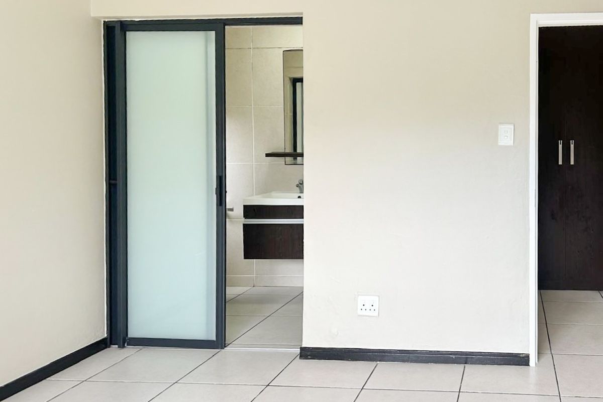 A bright, empty bedroom featuring tiled floors, a modern sliding frosted glass door leading to an en-suite bathroom, and a built-in cupboard.