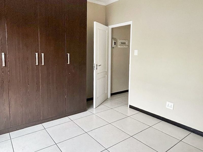 A clean, empty bedroom featuring neutral tiled flooring, built-in dark wood cupboards, and a simple pendant light fixture.