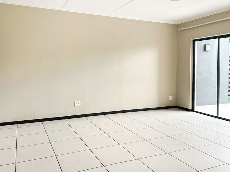 A bright, empty living area featuring neutral tiled flooring and a sliding glass door providing access to an outdoor space.
