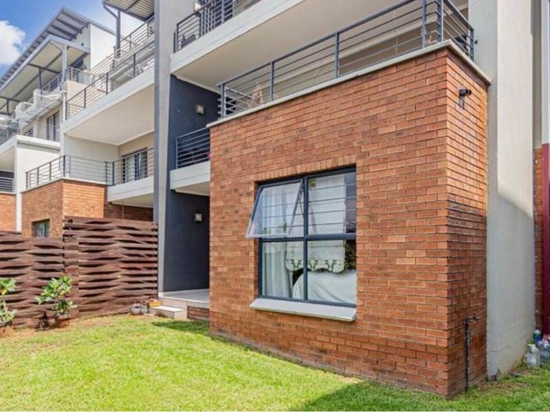 Rear view of the apartment building featuring exposed brickwork, a private balcony with metal railings, and a small garden area.