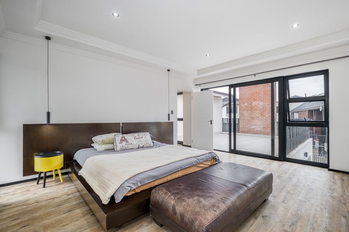 Spacious bedroom featuring modern laminate flooring, recessed lighting, crown molding, and large sliding glass doors opening onto a private balcony.