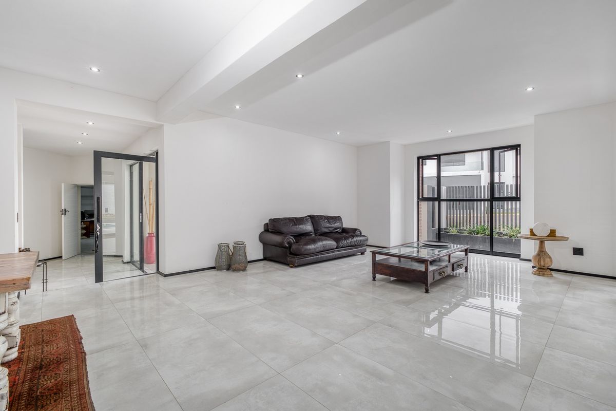 Spacious living area featuring large format polished floor tiles, recessed downlighting, and modern black aluminium framed windows and doors.