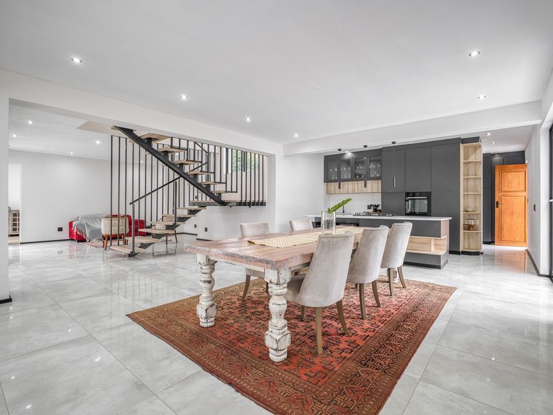 Modern open-plan living area featuring a contemporary kitchen with dark cabinetry, a central island, and a striking architectural staircase.