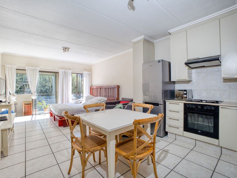 Open-plan studio apartment featuring a compact kitchen with built-in cabinetry, tiled flooring throughout, and direct access to a balcony through sliding glass doors.