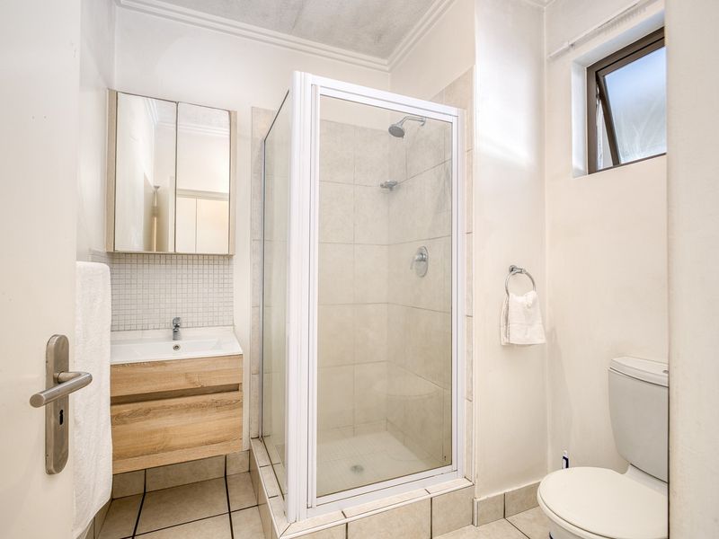 A compact bathroom featuring a glass shower enclosure, a modern wood-finish vanity with basin, and a standard toilet.