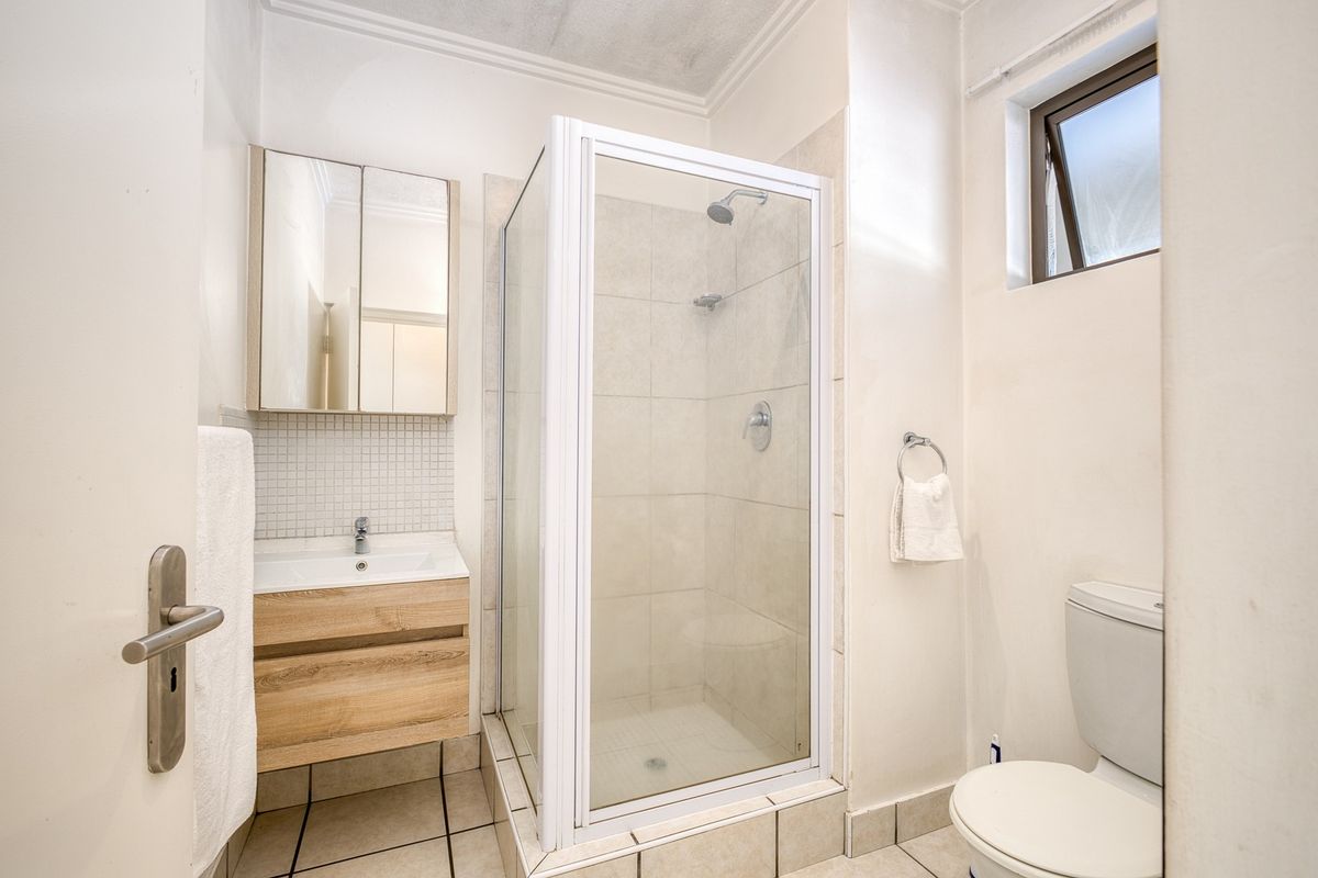 A compact bathroom featuring a glass shower enclosure, a modern wood-finish vanity with basin, and a standard toilet.