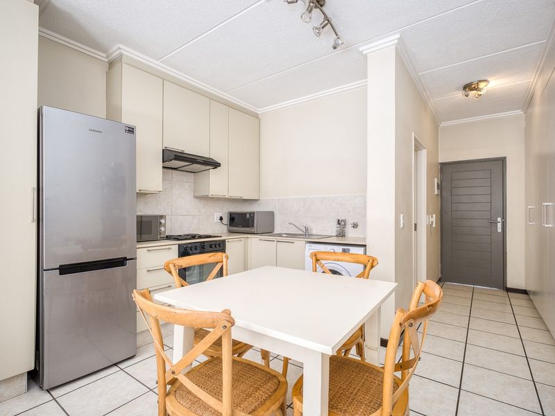 Open-plan kitchen and dining area featuring tiled flooring, built-in cabinetry, and integrated appliances, providing a functional and compact living space.