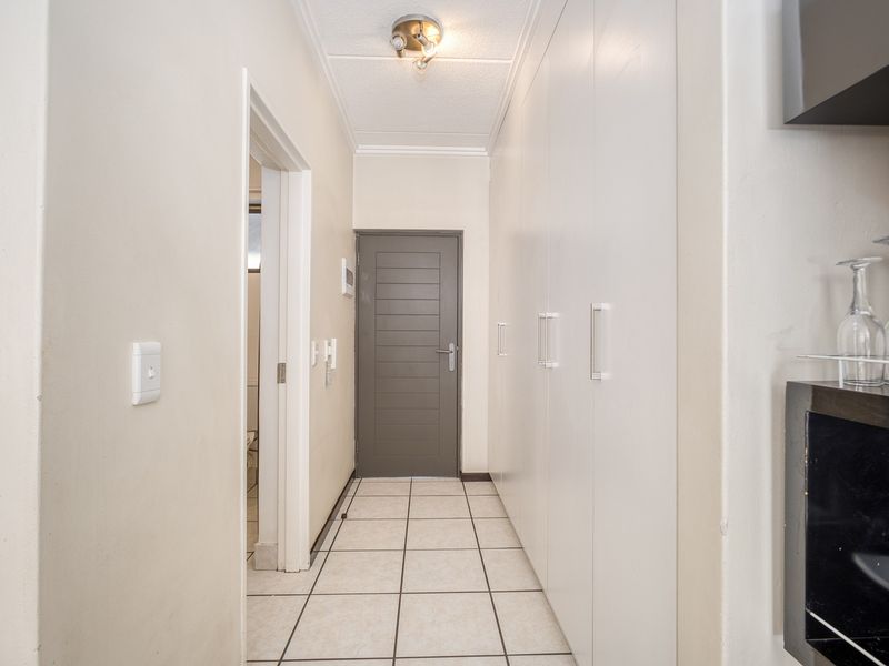 A clean, well-lit hallway featuring neutral tiled flooring and extensive built-in storage cupboards, leading to an internal room.