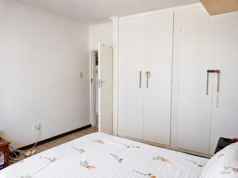 A bedroom featuring built-in cupboards, laminate flooring, and neutral white walls, offering a clean and functional space.