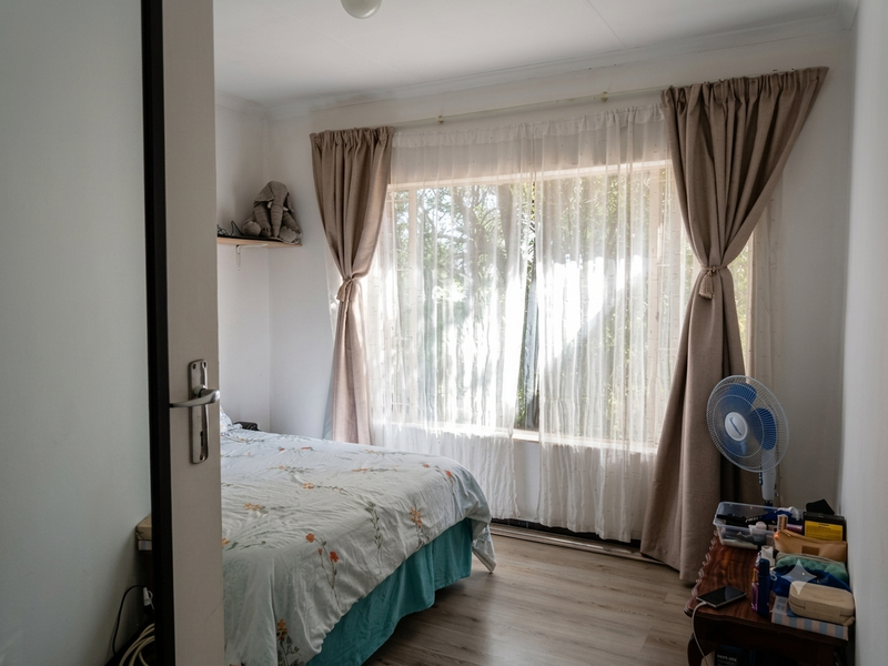 A bright bedroom featuring laminate flooring and large windows with curtain tracks, offering a functional space with natural light.