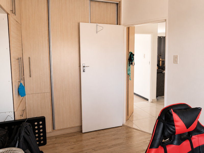 A bedroom featuring light wood-finish built-in cupboards, laminate flooring, and a doorway leading to an adjacent living area.