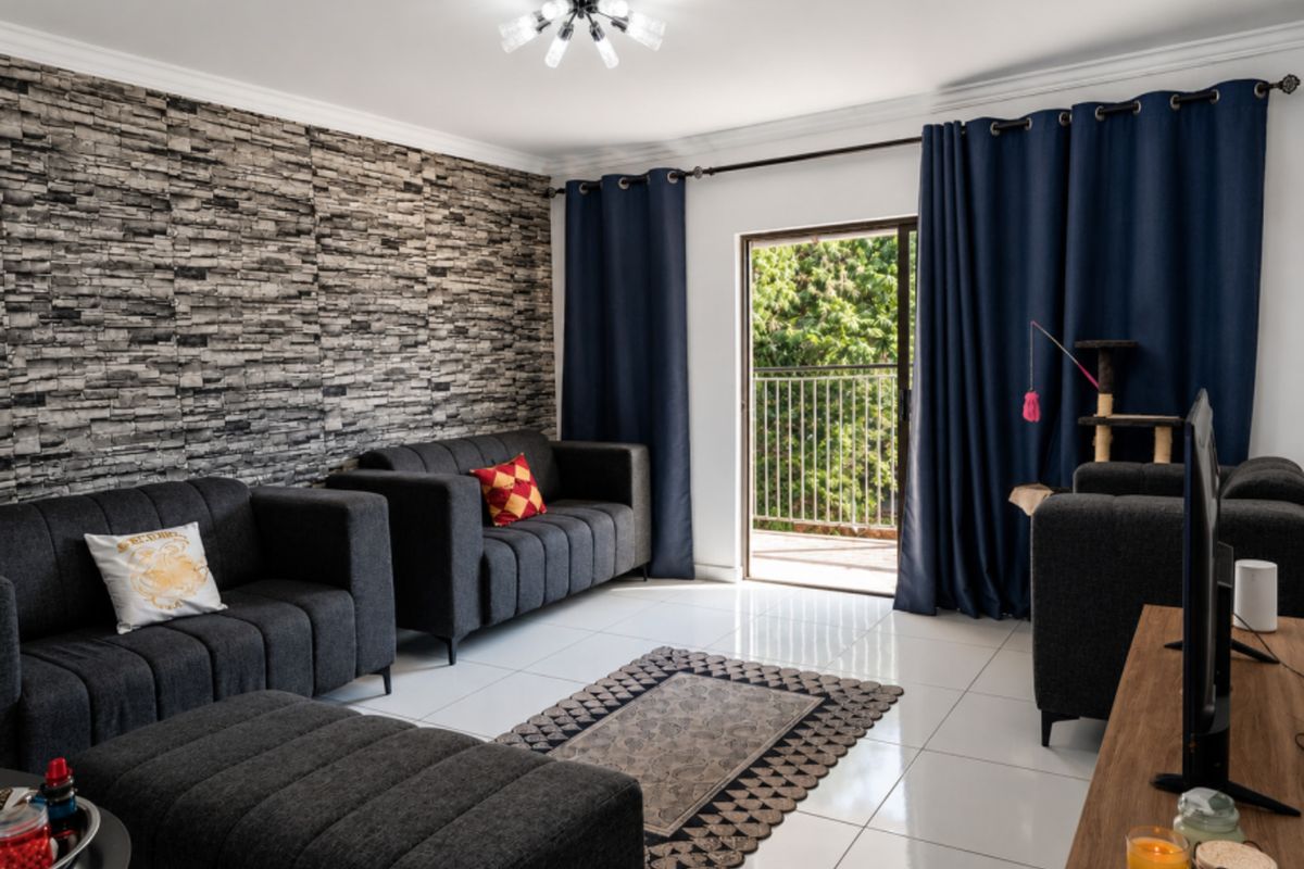 A well-maintained living room featuring a textured stone veneer accent wall, polished tile flooring, and direct access to a private balcony.