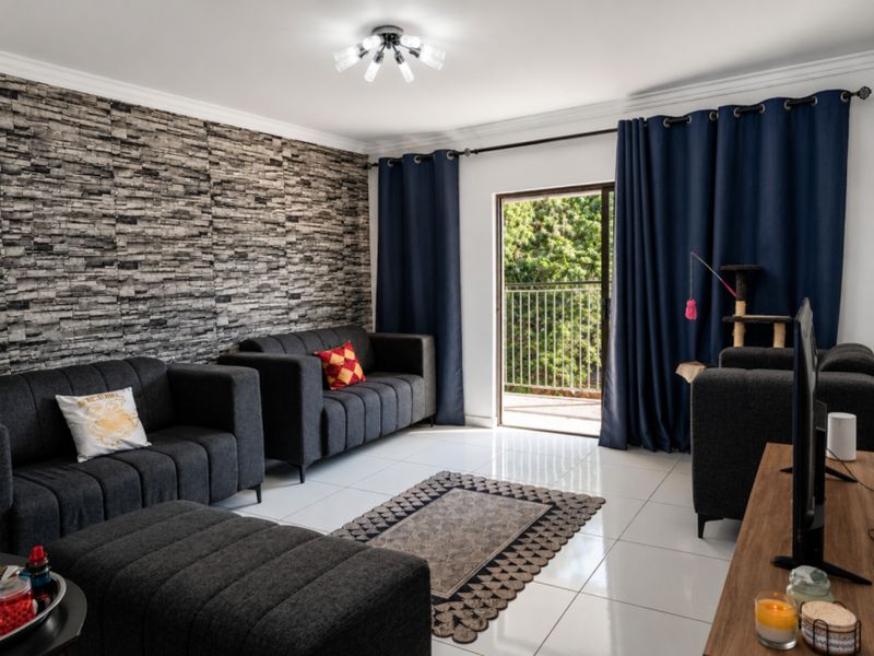 A well-maintained living room featuring a textured stone veneer accent wall, polished tile flooring, and direct access to a private balcony.