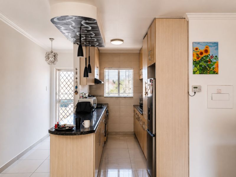 A functional kitchen featuring light wood cabinetry, granite countertops, a built-in hob, and tiled flooring, with direct access to an exterior security gate.