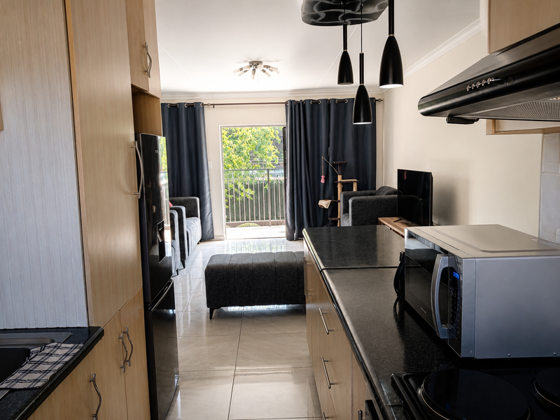 Open-plan kitchen and living area featuring modern cabinetry, granite countertops, tiled flooring, and direct access to a private balcony.