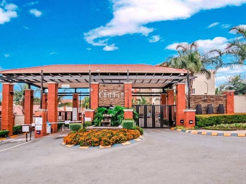 The secure main entrance gate of the apartment complex, featuring brick pillars, stone accents, and well-maintained landscaping.