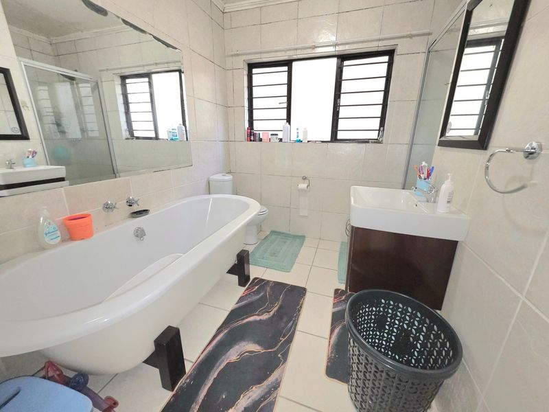 A functional bathroom featuring a freestanding bathtub, wall-mounted vanity, and tiled finishes, offering a practical layout with natural light from the window.
