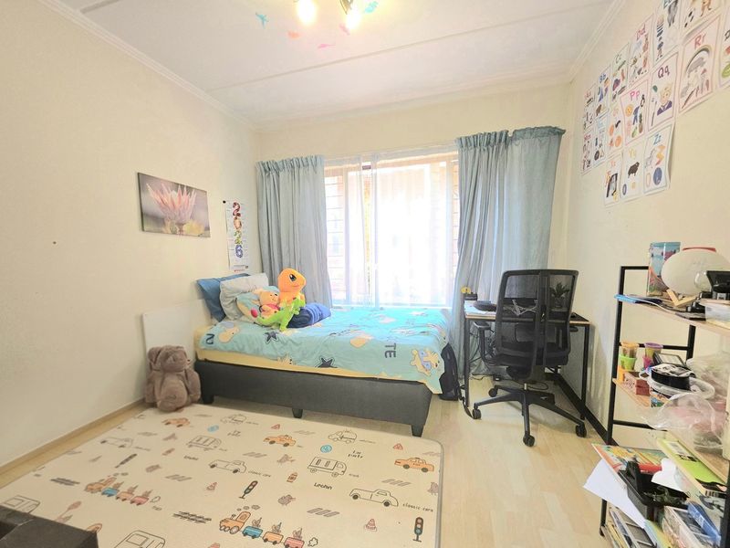 A functional bedroom featuring laminate flooring, neutral walls, and a large window with curtain rails, providing a bright and comfortable living space.