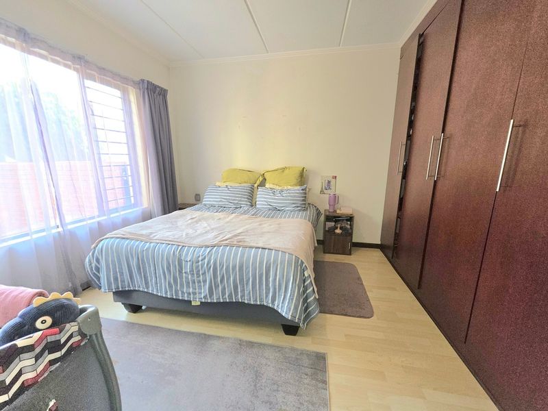 A bedroom featuring laminate flooring and floor-to-ceiling built-in cupboards, with natural light provided by a large window fitted with security bars.