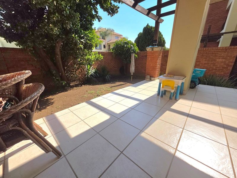 A covered patio area featuring tiled flooring, a brick boundary wall, and a timber pergola, overlooking a small garden space.