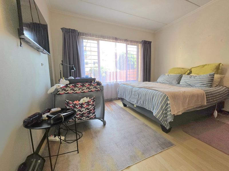 A functional bedroom featuring laminate flooring and a large window fitted with security bars, providing natural light and ventilation.