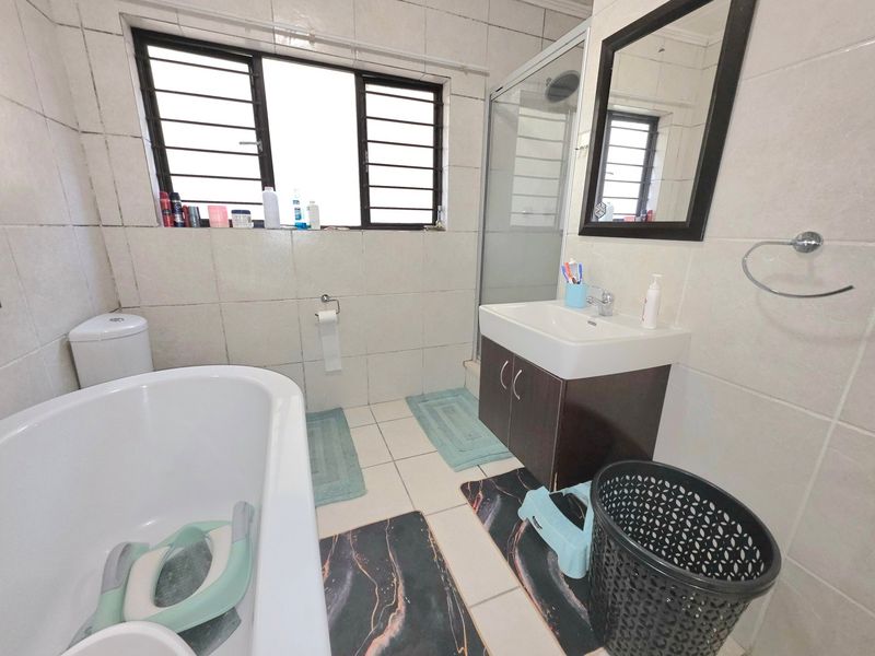 A functional bathroom featuring a freestanding bathtub, a separate shower enclosure, and a vanity cabinet with a basin, finished with tiled walls and floors.