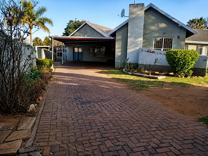 Front exterior view of a house featuring a paved driveway, attached carport, and a prominent chimney, with visible exterior wall maintenance required.
