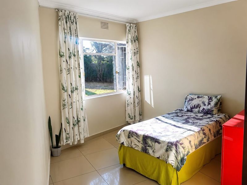 A functional bedroom featuring tiled flooring and a steel-framed window with natural light.