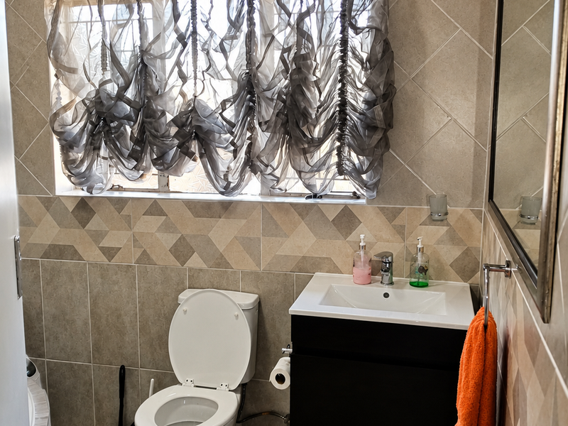 A functional bathroom featuring a wall-mounted vanity with a basin, a toilet, and neutral-toned tiled walls and flooring.