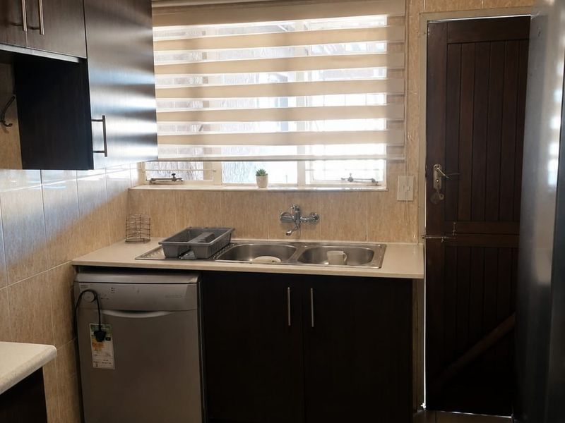 A functional kitchen area featuring dark cabinetry, double bowl sink, tiled splashbacks, and direct access to an exterior door.