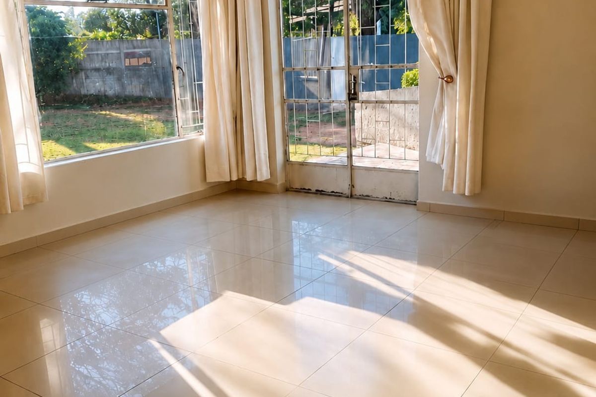 A bright and spacious living area featuring polished tile flooring, large windows, and a security gate leading to the garden.