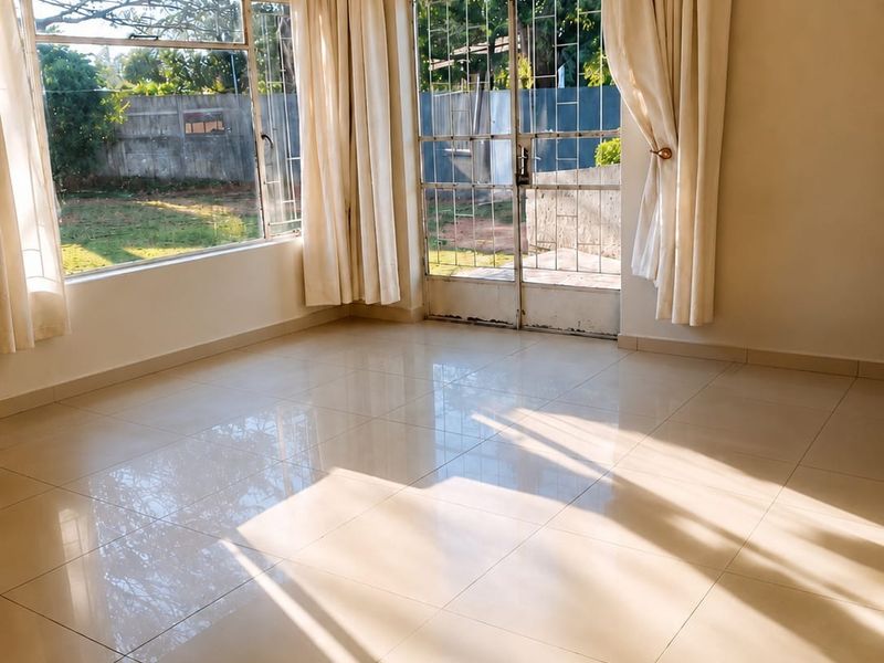 A bright and spacious living area featuring polished tile flooring, large windows, and a security gate leading to the garden.