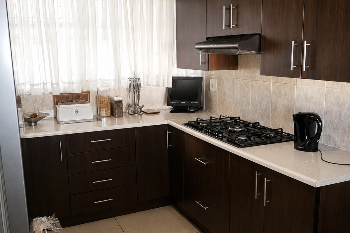 A functional kitchen featuring dark wood cabinetry, stone-look countertops, a gas hob with extractor fan, and neutral tiled flooring.