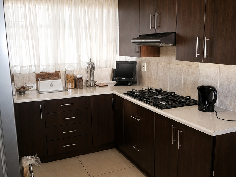 A functional kitchen featuring dark wood cabinetry, stone-look countertops, a gas hob with extractor fan, and neutral tiled flooring.