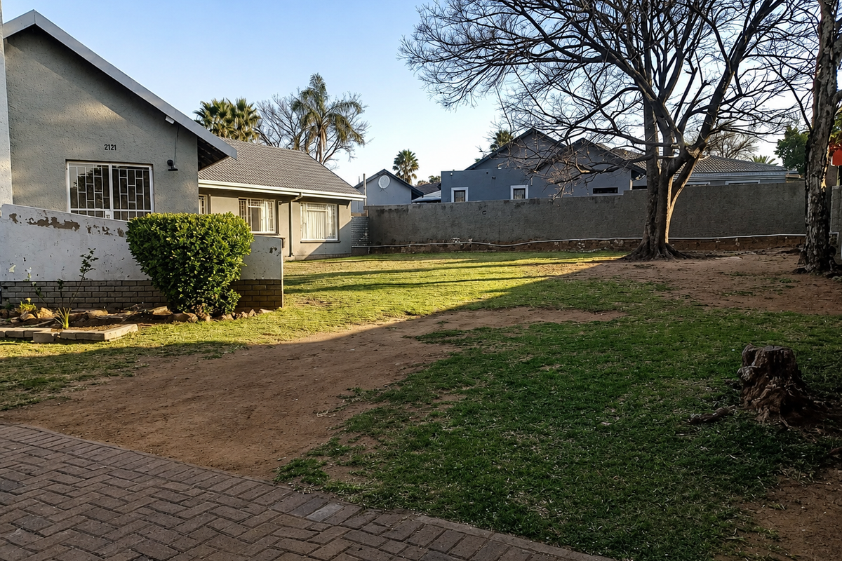Spacious rear garden featuring a paved driveway, perimeter walling, and established trees, providing a private outdoor area for the property.