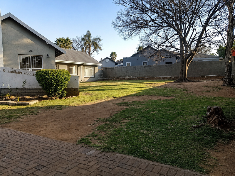 Spacious rear garden featuring a paved driveway, perimeter walling, and established trees, providing a private outdoor area for the property.
